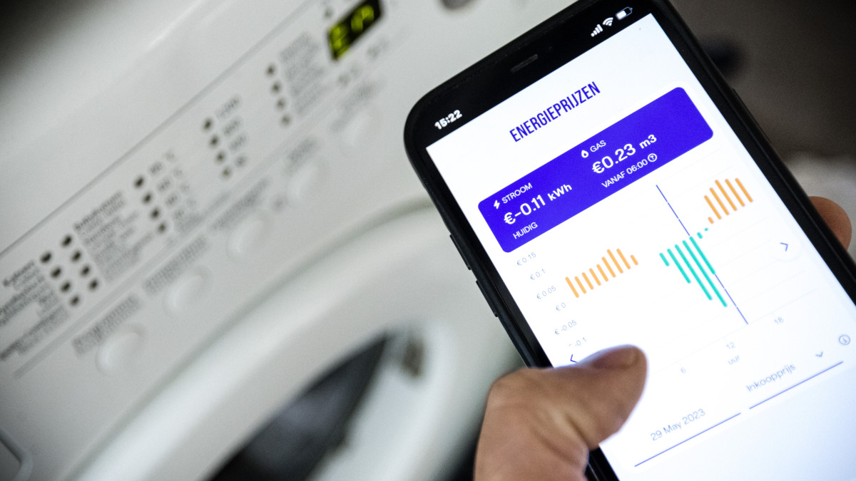 Een mobiele telefoon met de energietarieven van een dynamisch energiecontract bij een wasmachine. Beeld: ANP